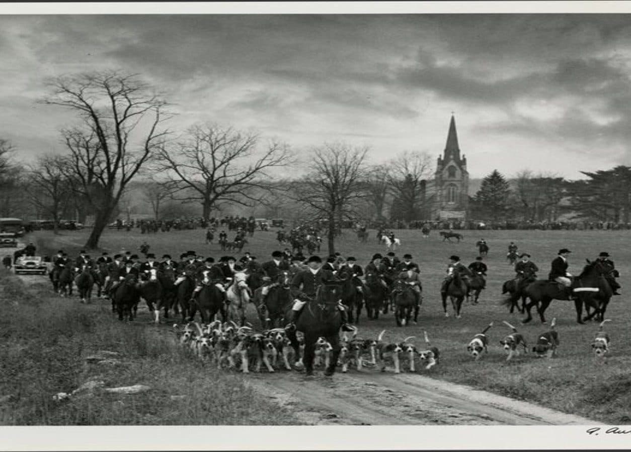 Historic photograph of a hunt gathering in the fields below the church